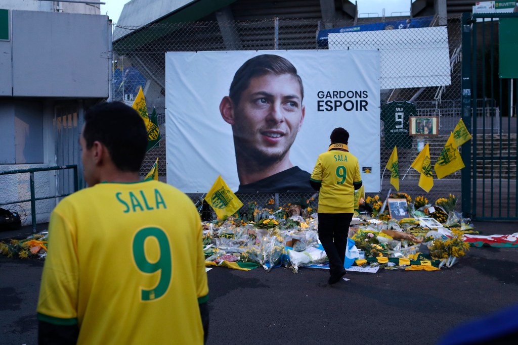 A man in a yellow football shirt with the number 9 and the word Sala on it stands in front of a tribute to a dead football player.
