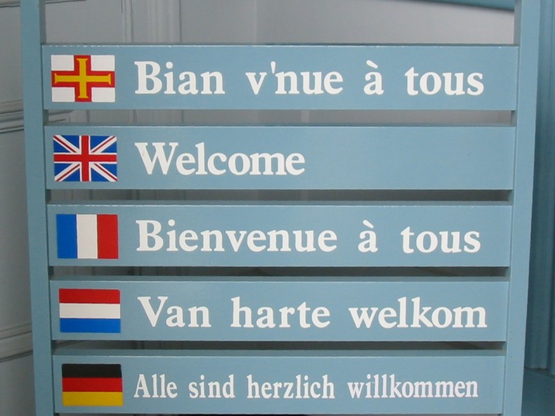 A sign with Welcome in various languages including Guernésiais. Bian v'nue a tous, Welcome etc.