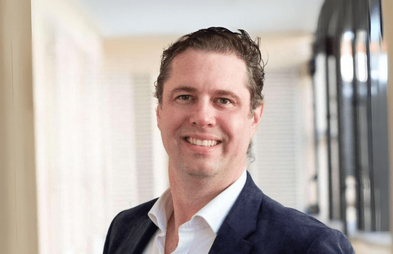 A smiling man in a suit with an open buttoned shirt.