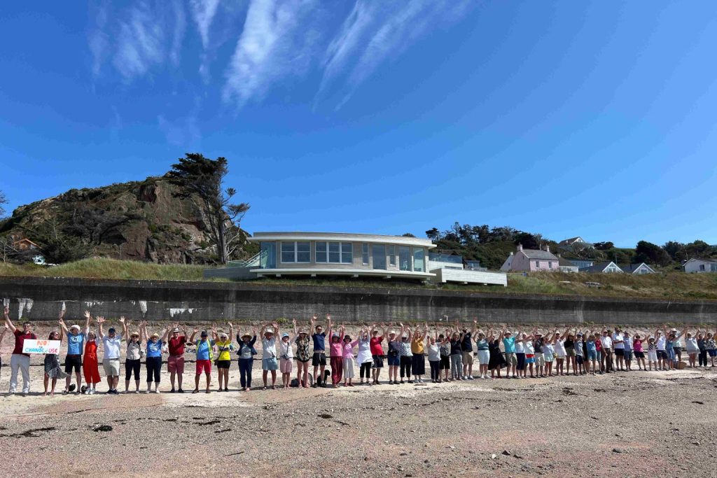 row of people holding up hands in protest on beach in front of nude dunes building