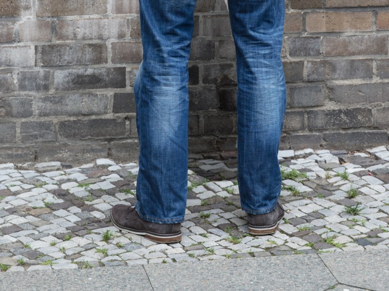 Rear View Of A Man In Hood Peeing On Wall In Street