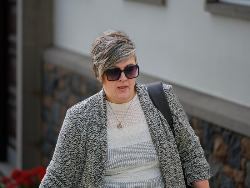 A woman with short grey hair and sunglasses walks up a hill.