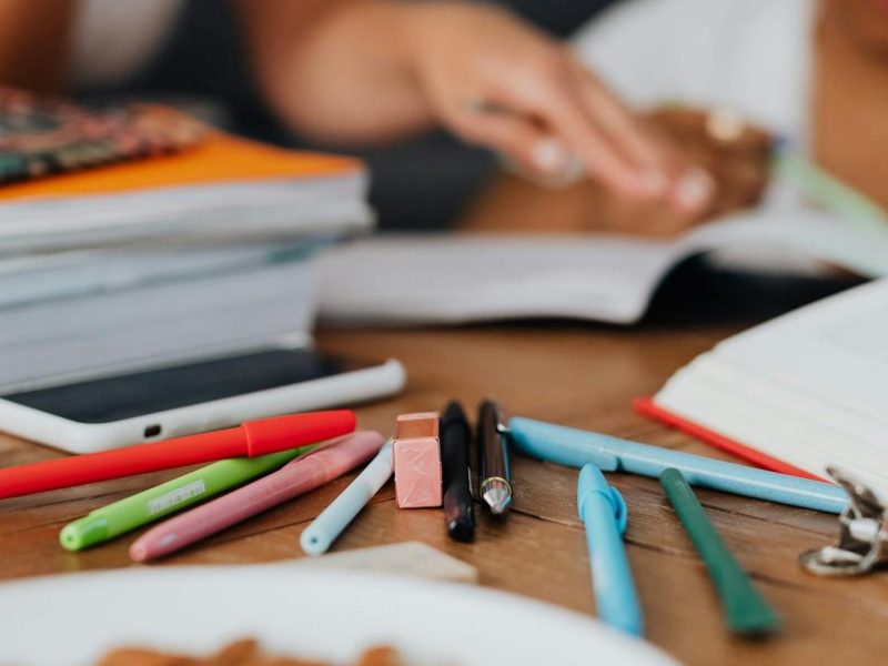 colorful pens near stack of books and cellphone on a wooden surface