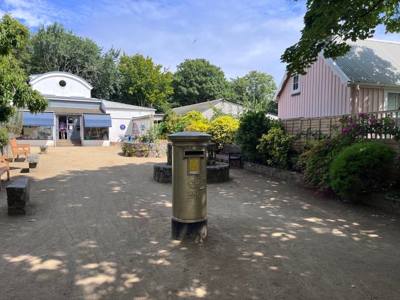 A golden postbox in Sark, close to shops and a cafe.