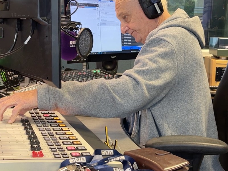 A grey-haired man presenting a radio show in a radio station.