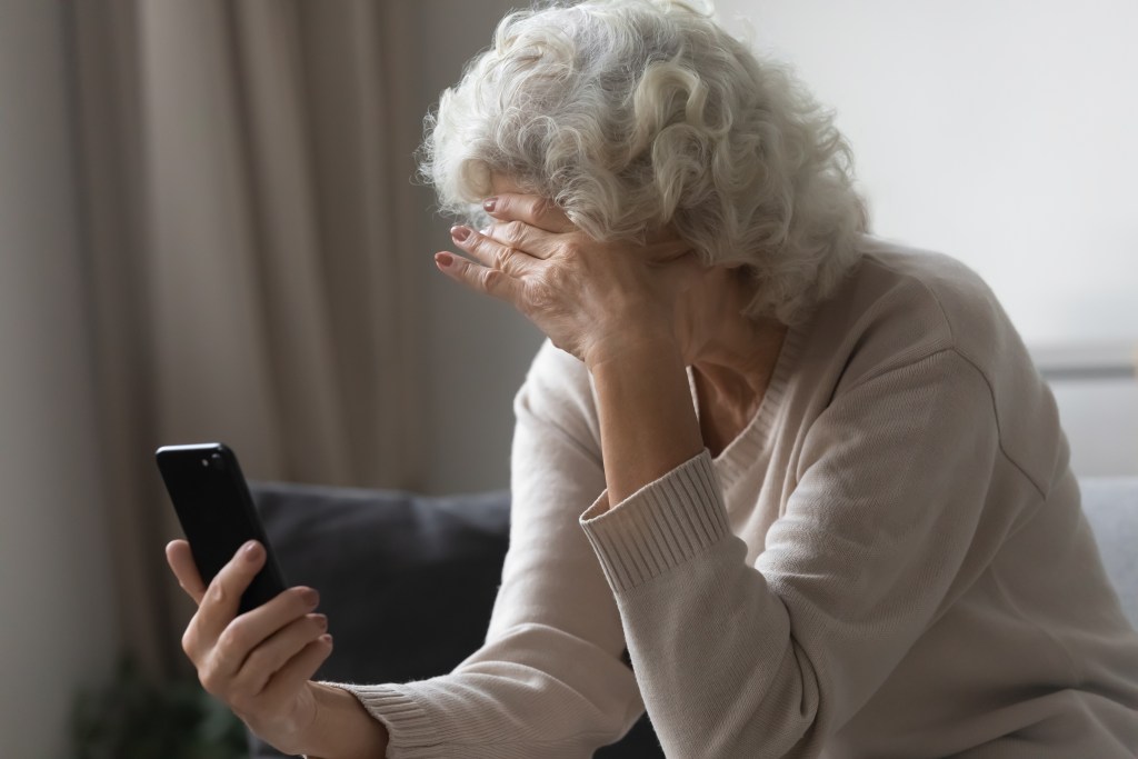 An old lady looks at her mobile phone with her head in her hands.