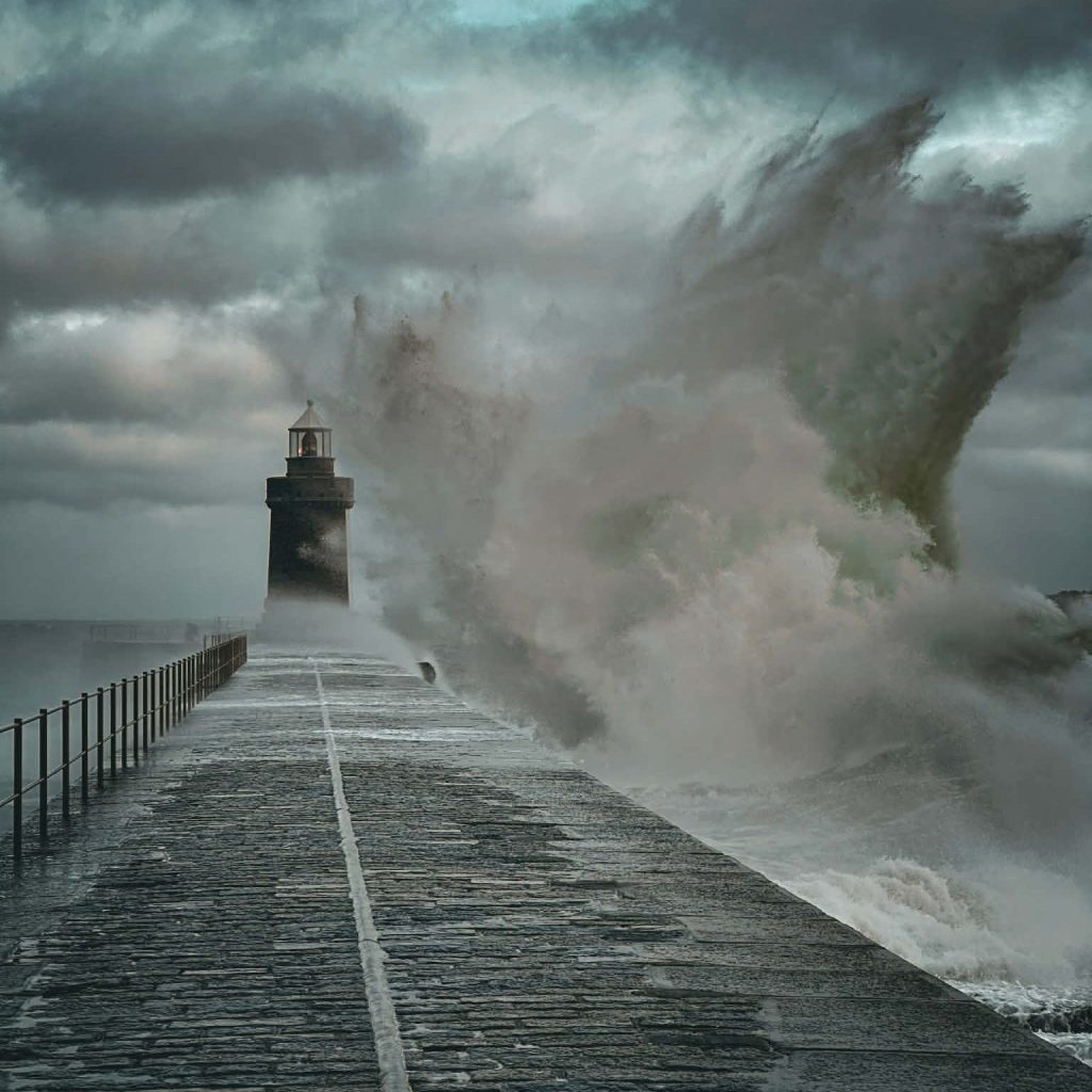 Waves crash over a breakwater and lighthouse in St Peter Port, Guernsey.