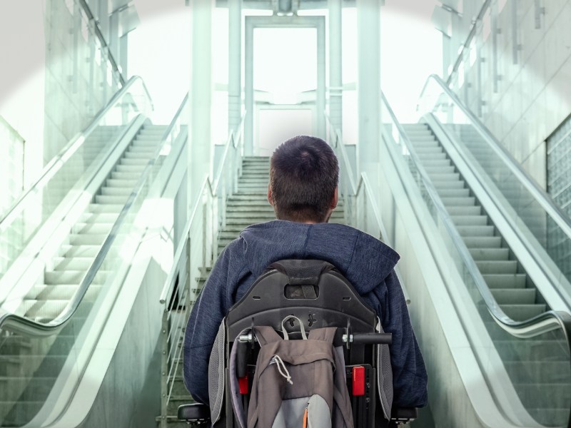 A man in a wheelchair looks up a flight of stairs.