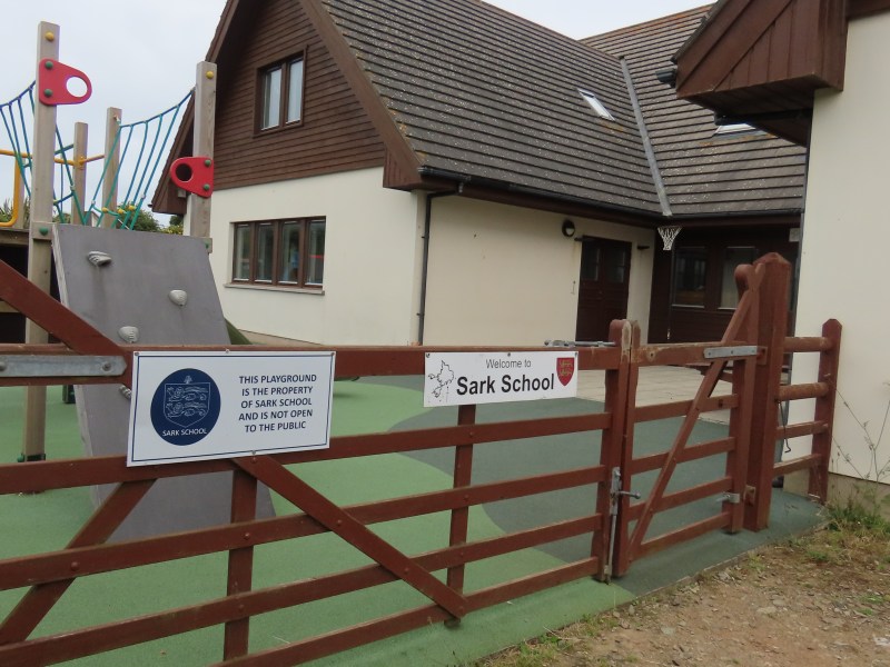 Sark School - a one-storey building with a gabled roof, and a children's play area outside.