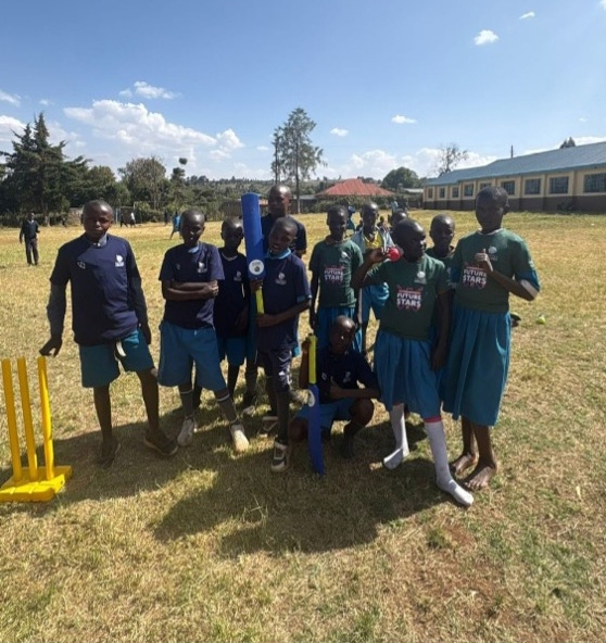 Kenyan children in two teams pose together with plastic cricket equipment on a sunny field.