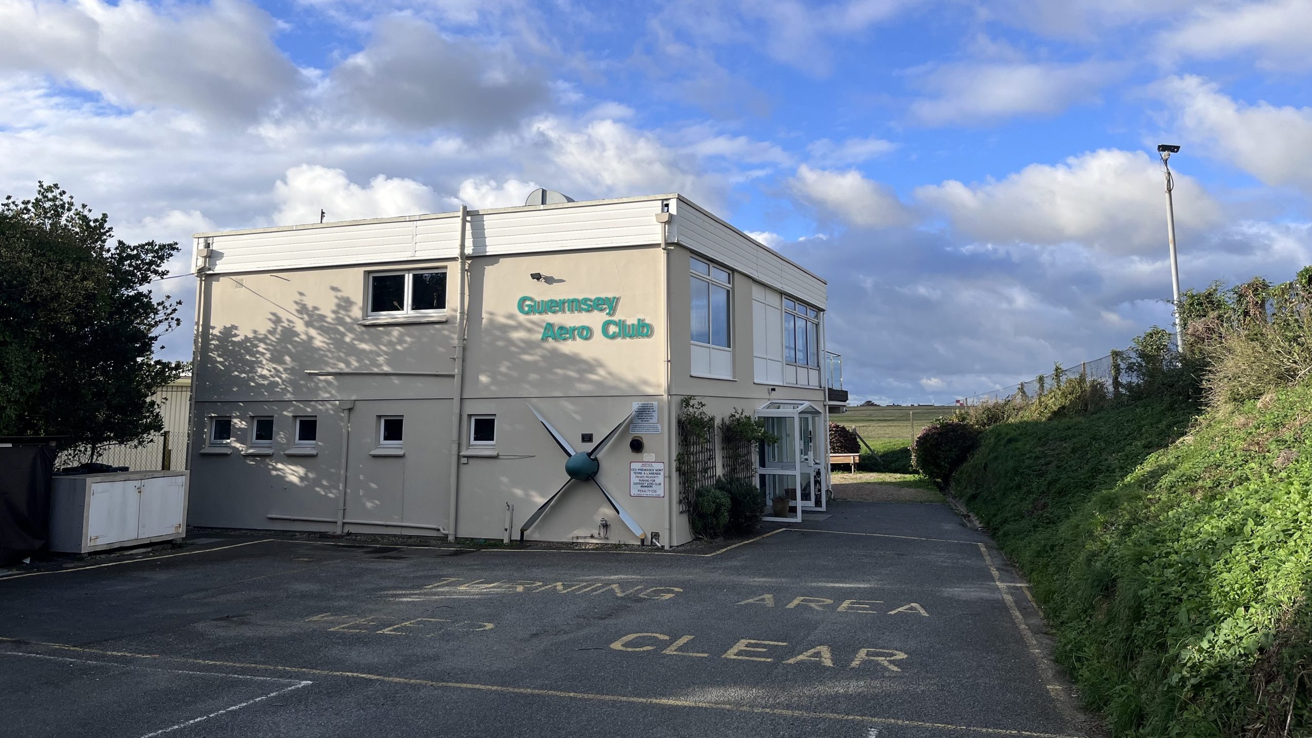 A two-storey building with a large aeroplane propellor on the side, and a green Guernsey Aero Club sign.