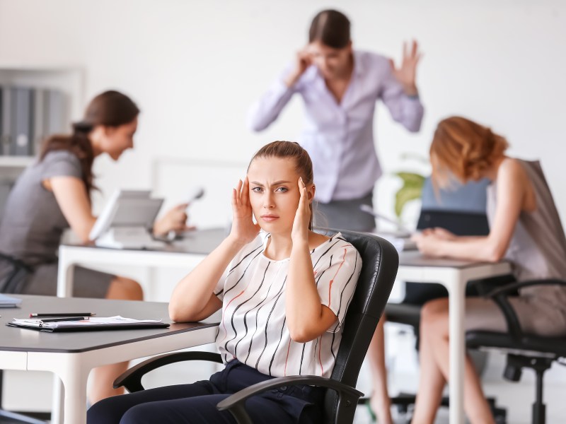 A woman puts her hands by her ears to block out the noise of her coworkers in a busy office.