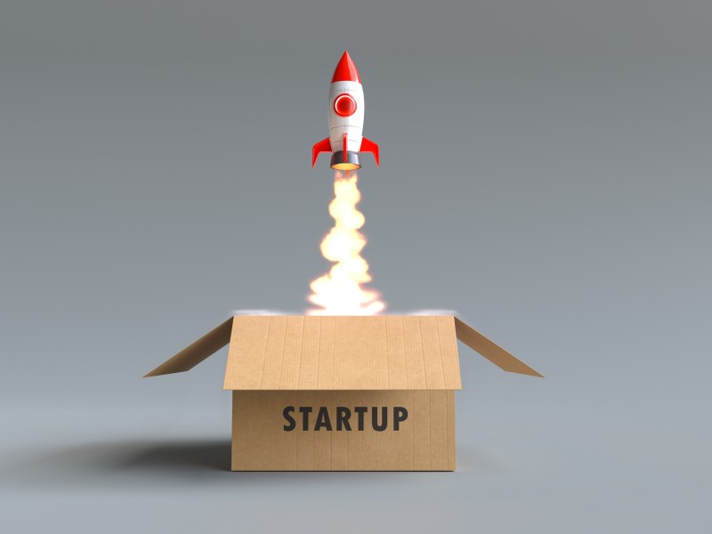 A child's rocket launches from a cardboard box that says Startup on the side. Fire comes out of the bottom of the rocket.