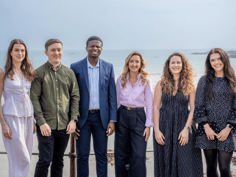 Several smartly-dressed younger professionals stand in front of the sea.