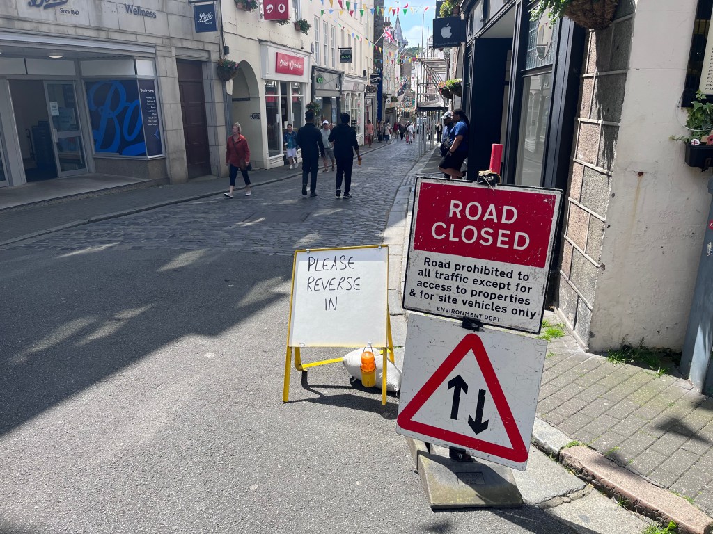 A road closed sign next to a street in St Peter Port. Another sign says please reverse in.