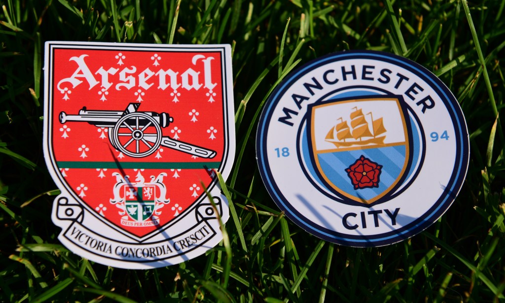 The Arsenal and Manchester City badges laid on some short grass.