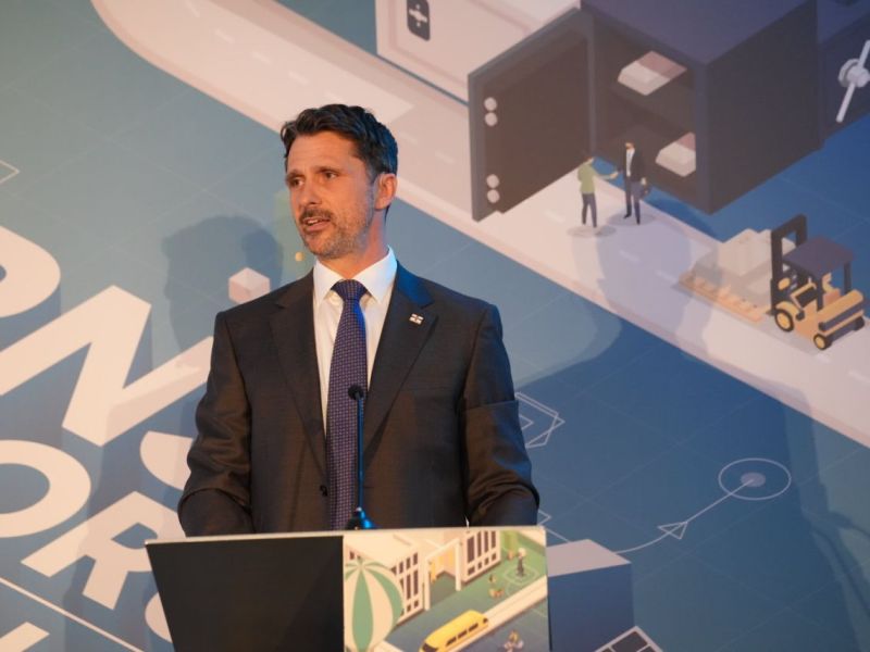 A man in a suit stands at a lectern.
