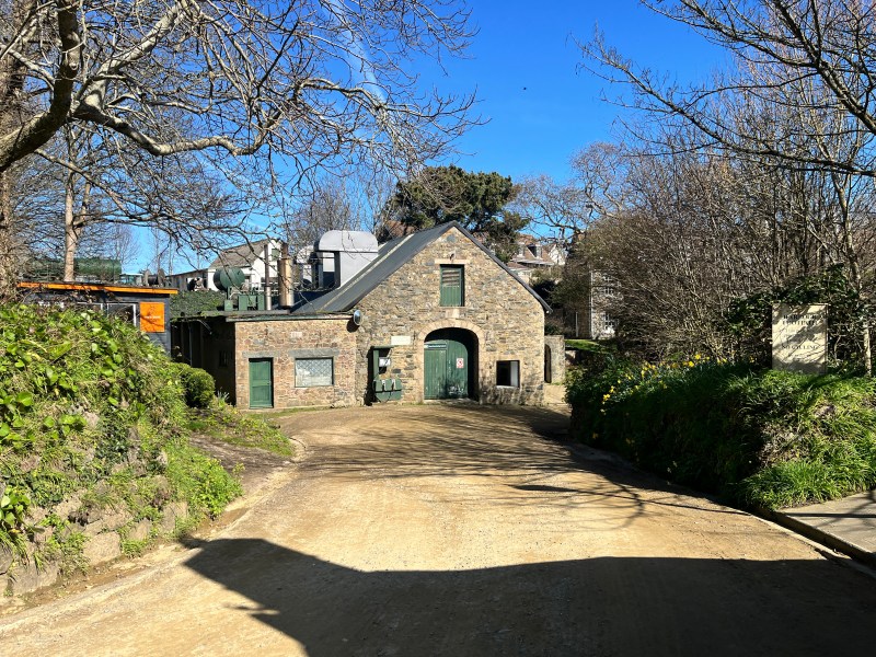 A granite building in front of a dirt track. Green signage says Sark Electricity Limited.