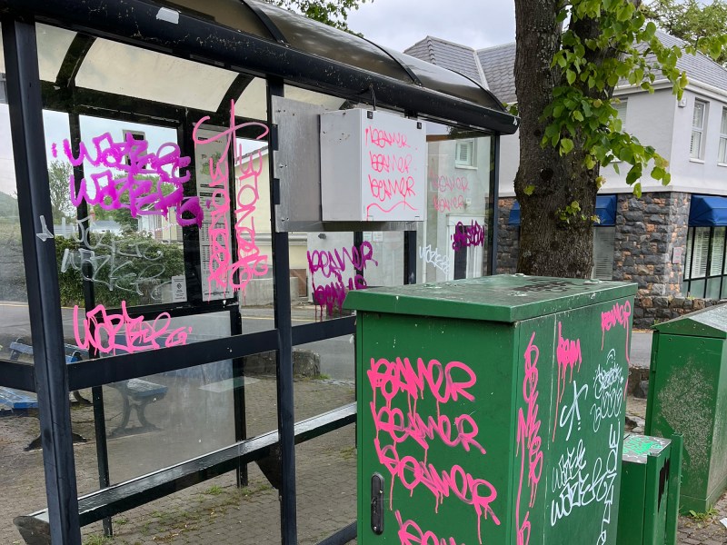 Graffiti on a bus stop and nearby electrical unit.