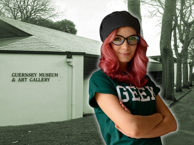 A woman with red hair, glasses, a beanie hat and a T-shirt that says Geek. She's superimposed in front of an image of Candie Museum and Art Gallery - a modern, one story museum building.