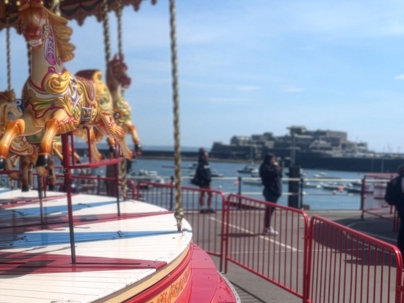 A traditional carrousel in front of a harbour with a castle in the distance.