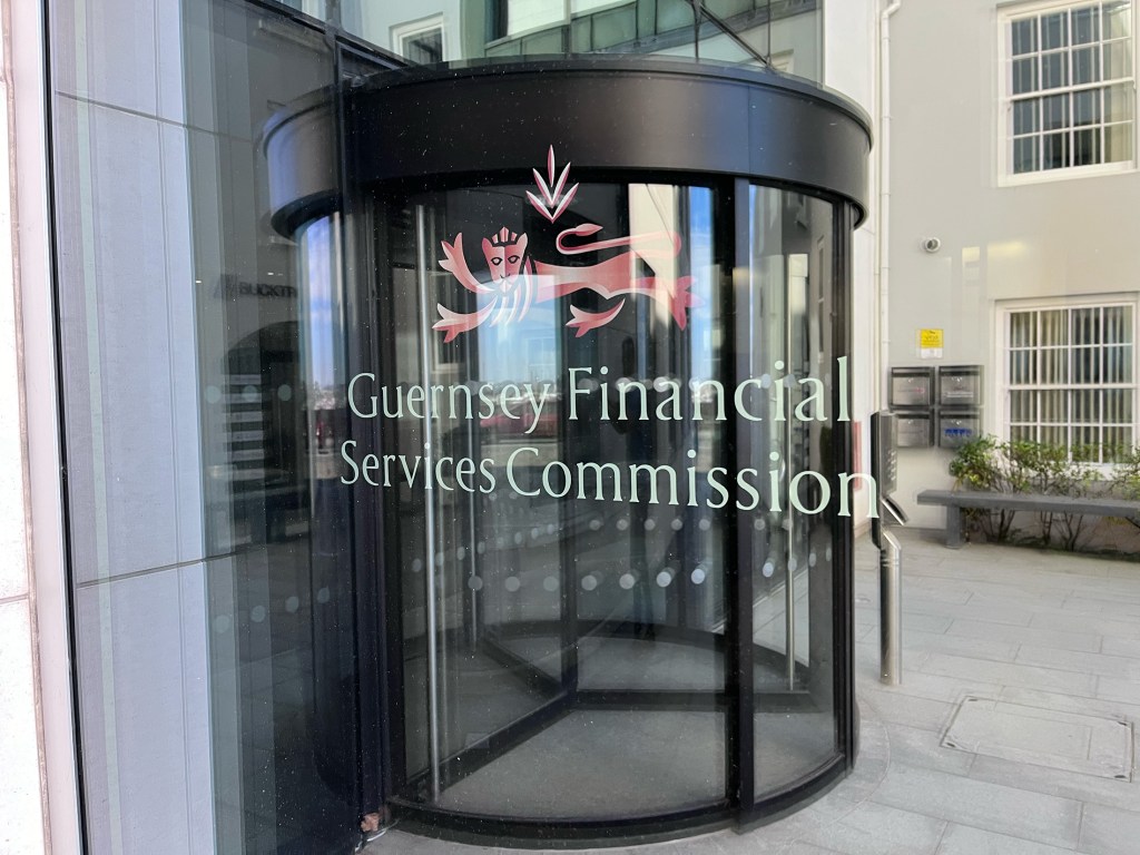 A logo reflected in a window, along with a revolving door. It says Guernsey Financial Services Commission and has a lion motif.