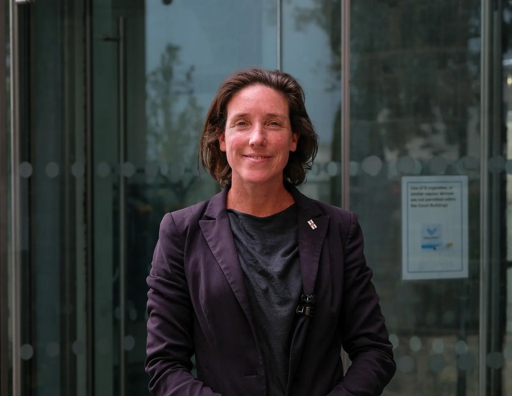 A woman in a dark blue business suit in front of some glass revolving doors.