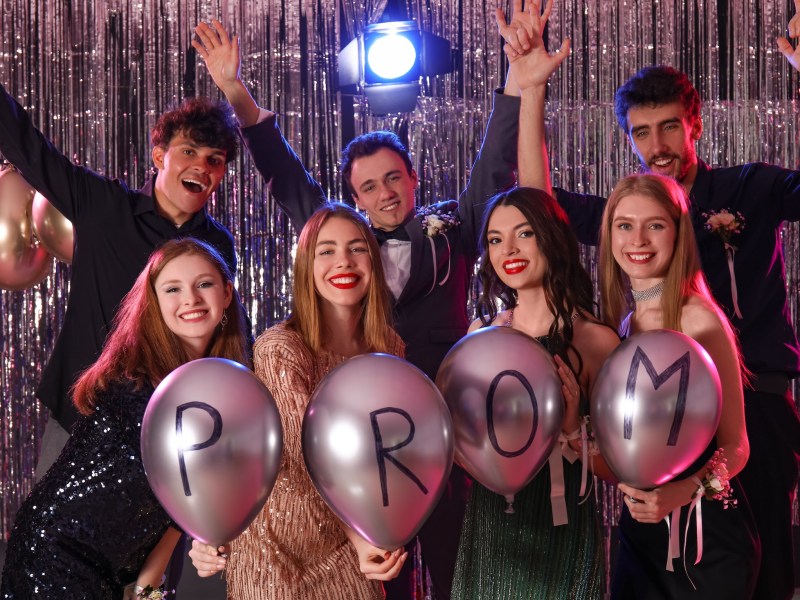 High school students posing for a photo at their prom, with balloons spelling out the word prom.