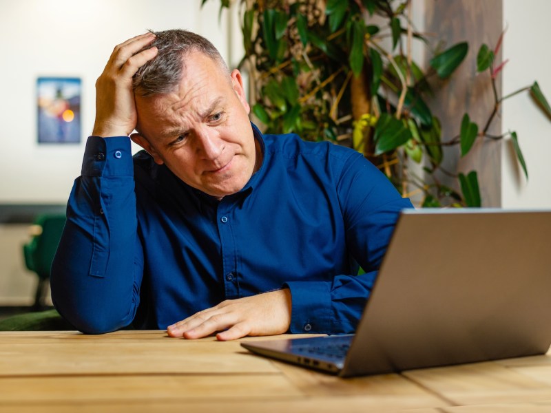 Man scratches his head in confusion while sitting in front of his laptop.