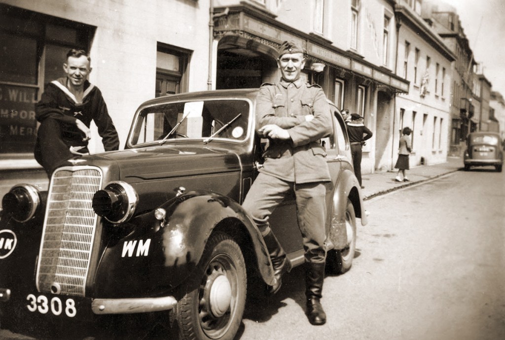 Sepia photo of two men in German military uniforms by a car in Guernsey.