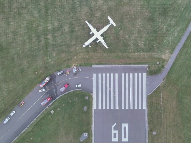 A aerial shot of plane on the grass next to a runway.