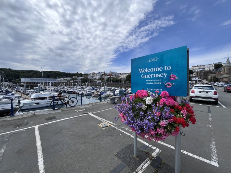 A harbour full of boats, with a Welcome to Guernsey sign and bright flowers.