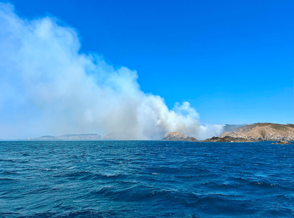 Smoke billows over the sea from a small island.