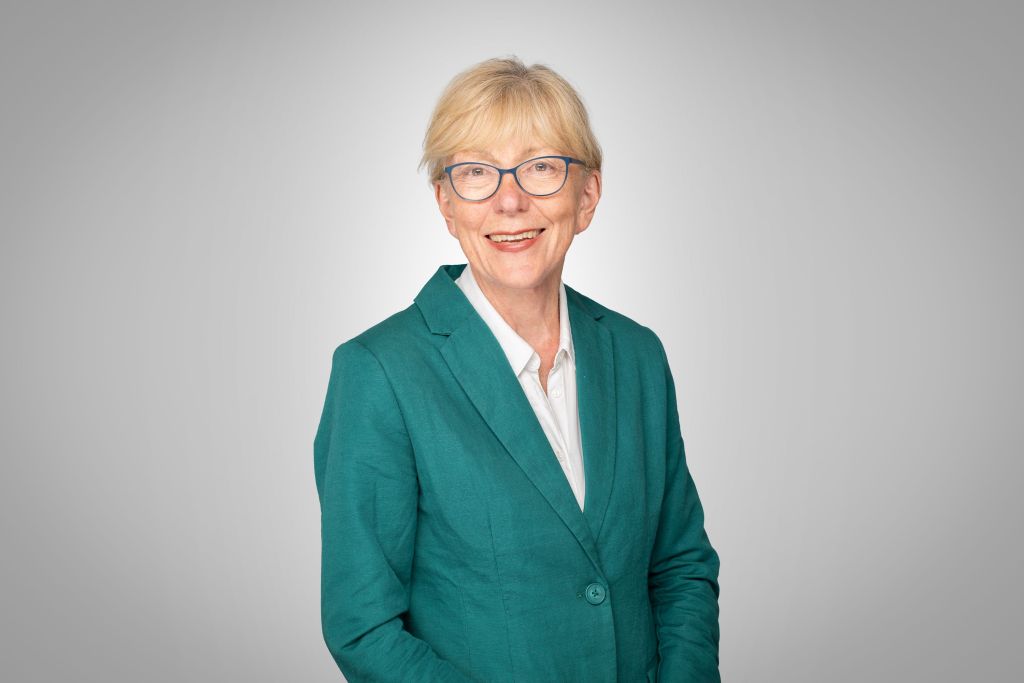 A woman with short fair hair and glasses in a green jacket.
