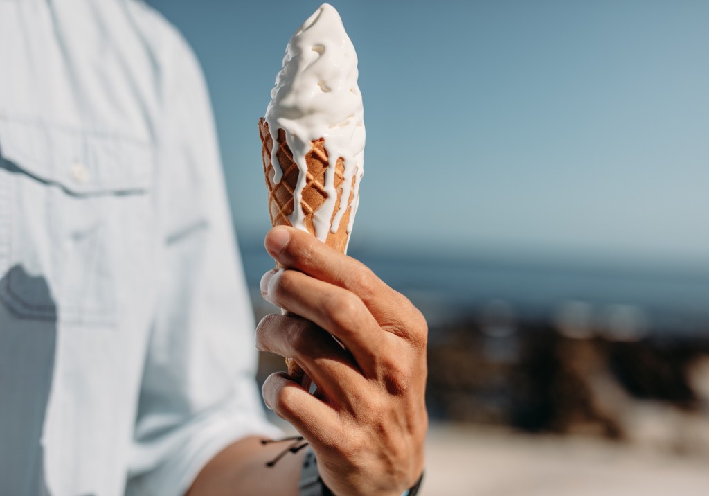 Close up of hand of man holding a melting ice cream cone. Man holding an ice cream on sunny day.
