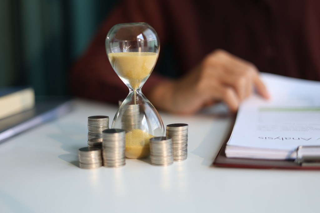 Coin stacks and sand clock on the table. Growing of income, saving or return investment through time. Time and money concept.