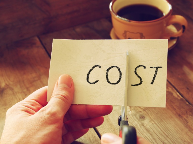A man cuts a post it note that says 'cost'.