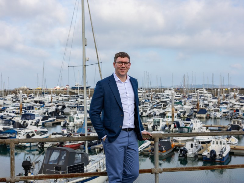 A man stands in front of town harbour which is full of boats
