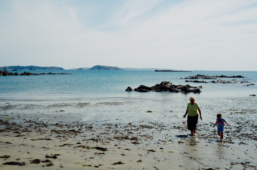 St. Peter Port , Guernsey - old elderly senior woman grandmother gathering sea shells with her grand daughter