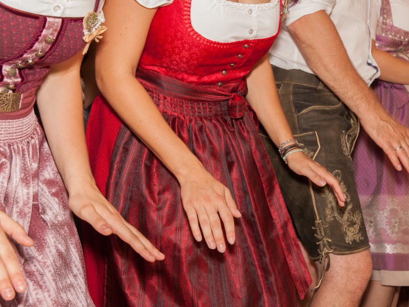 A group of people from the shoulders down wearing traditional lederhosen and dirndls dancing