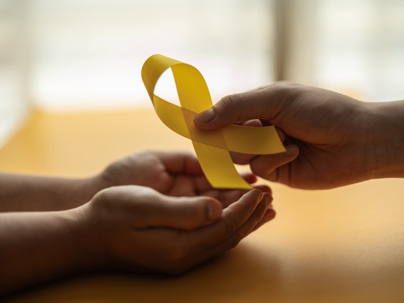 hands giving yellow ribbon to sick person suffering from cancer, world cancer day, healthcare and medicine backdrop, suicide prevention, children health care.