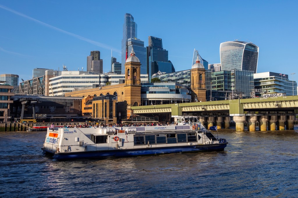 London, UK - April 29th 2025: A tourboat on the River Thames in London, UK, with Cannon Street Railway Station behind.