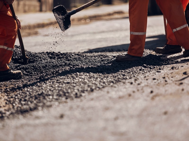 Construction worker working on a new asphalt layer on a public street.