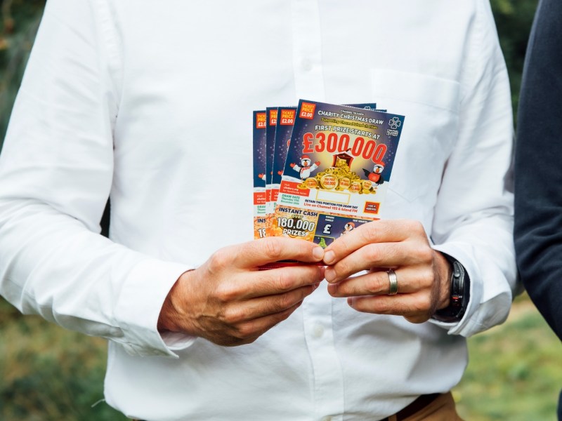 A man is shown from the shoulders down in a white shirt holding some lottery tickets