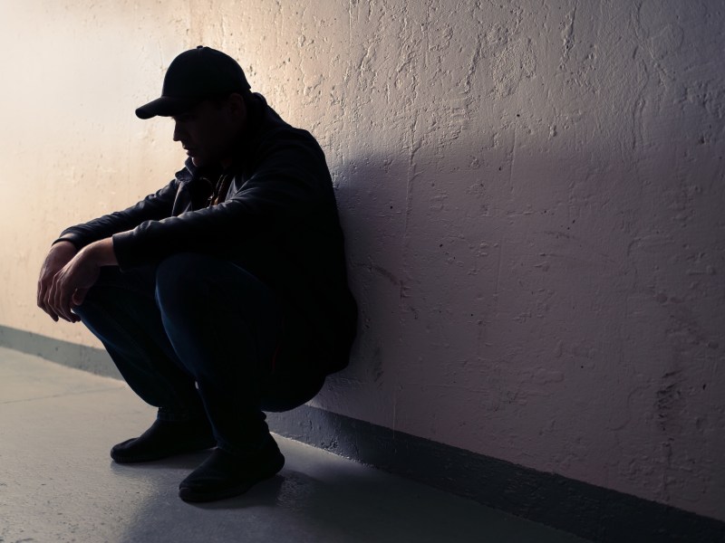Silhouette of a homeless person crouched and leaning against a wall.