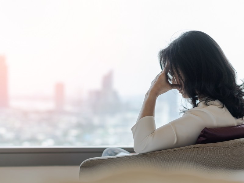 Anxiety disorder menopause woman with mental health illness, stressful depressed aging businesswoman female person with headache and migraine sitting tiredly at home with city background